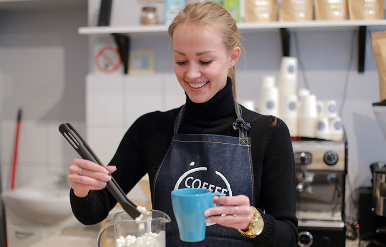 青いカップにコーヒーを入れる女性店員